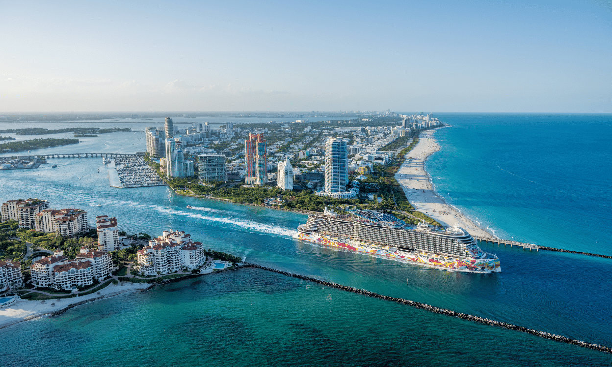 Kreuzfahrtschiff der Norwegian Cruise Line fährt aus dem Hafen von Miami, umgeben von Hochhäusern und Stränden. Kreuzfahrtschiff der Norwegian Cruise Line fährt aus dem Hafen von Miami, umgeben von Hochhäusern und Stränden.